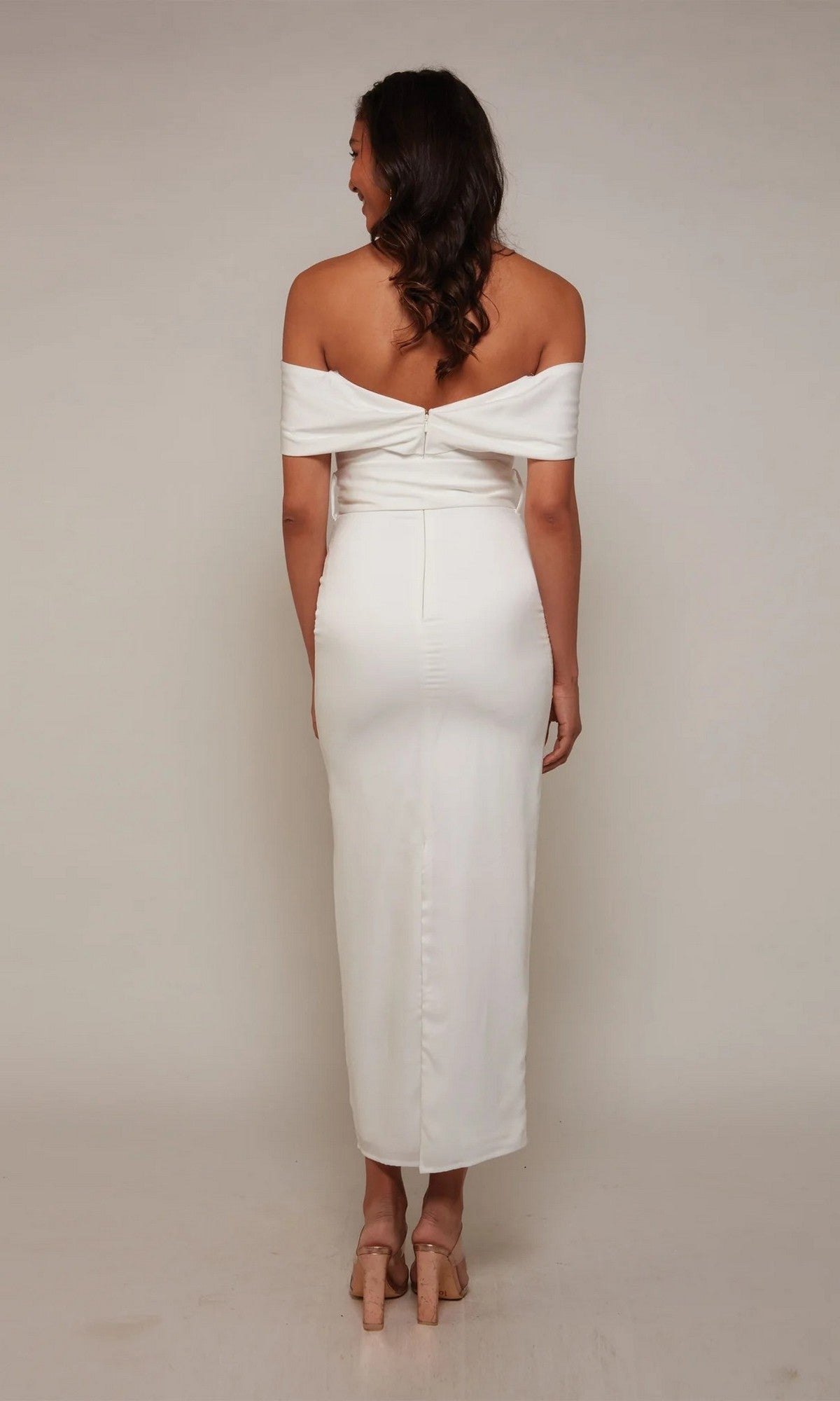 A woman stands with her back to the camera, wearing the Tea Length Formal Dress: Alyce 70041 and beige heels against a plain light-colored background.